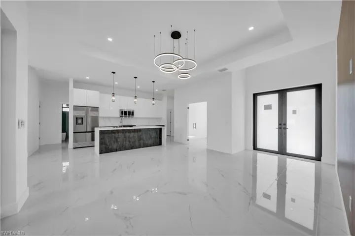 Unfurnished living room with french doors, hanging lights, light marble finish flooring, and a tray ceiling