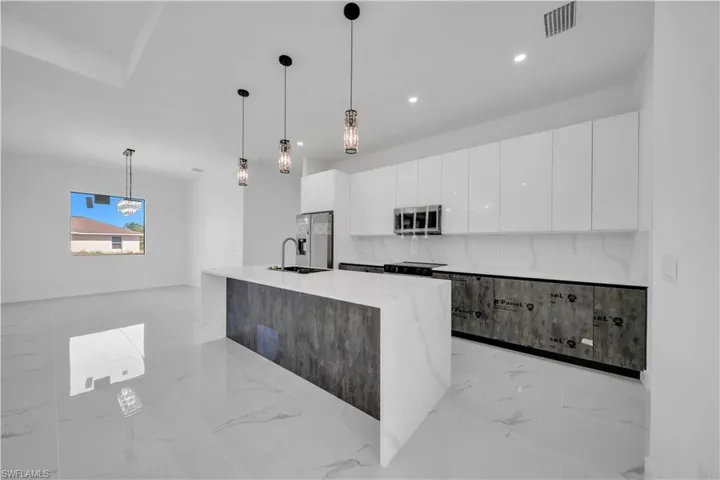 Kitchen featuring light stone countertops, modern cabinets, decorative light fixtures, stainless steel appliances, and light marble finish floors