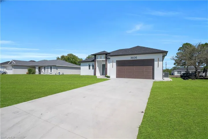 Prairie-style home featuring a front lawn, driveway, an attached garage, and stucco siding