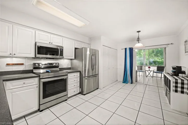 Kitchen featuring appliances with stainless steel finishes, white cabinetry, light tile patterned floors, decorative light fixtures, and ornamental molding leading to the screened lanai.