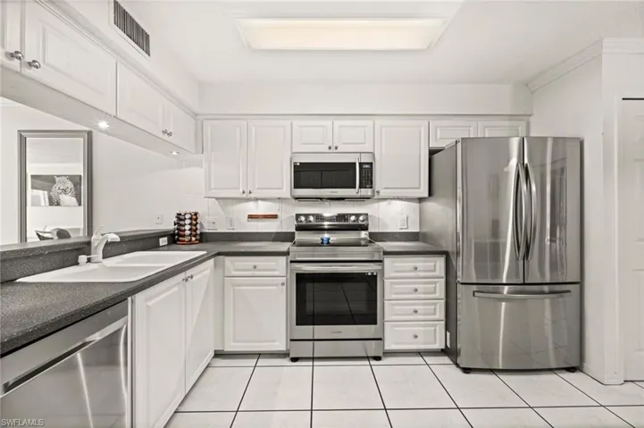 Kitchen with stainless steel appliances, countertops, white cabinets, and light tile patterned floors