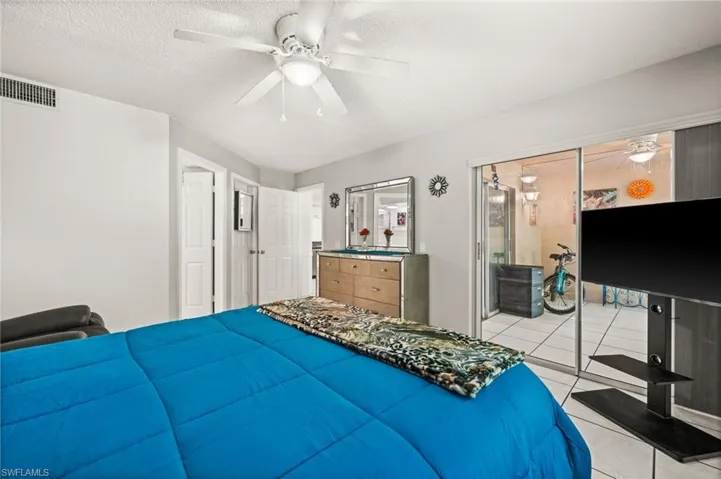 Primary Bedroom leading to the screened Lanai with light tile patterned floors, and a ceiling fan.