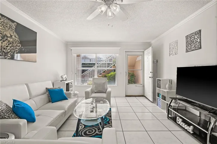 Living area with ornamental molding, tile patterned flooring, a textured ceiling, and ceiling fan