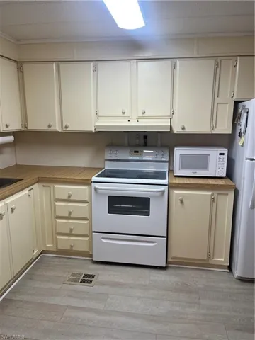 Kitchen featuring electric range, light countertops, refrigerator, exhaust hood, and light wood finished floors