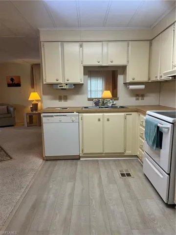 Kitchen with stove, white dishwasher, light wood-type flooring, open floor plan, and light countertops