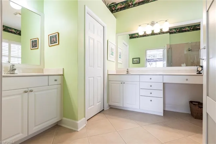Full bath with light tile patterned flooring, two vanities, and a stall shower