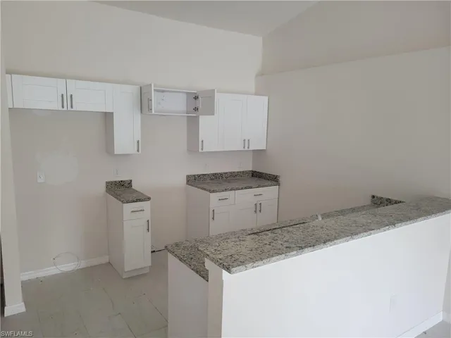 Kitchen with light stone counters, kitchen peninsula, white cabinets, and light tile floors