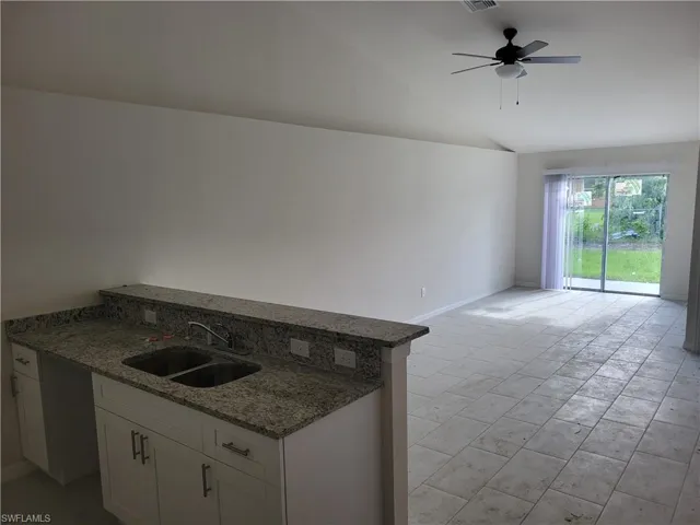 Kitchen featuring light tile flooring, ceiling fan, white cabinets, sink, and lofted ceiling