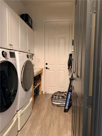 Laundry area featuring light wood-finish flooring, white paneled cabinetry with silver hardware, and a built-in wooden shelving unit