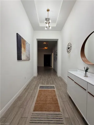 Hallway featuring wood-finish flooring, recessed ceiling with a modern pendant light, white walls, and a built-in console cabinet with integrated handles