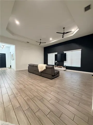 Spacious interior featuring wood-finish flooring, tray ceilings with recessed lighting, and modern ceiling fans