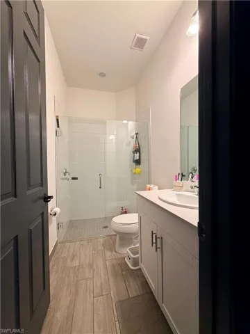 Bathroom featuring wood-finish plank tile flooring, a glass-enclosed shower with white subway tile surround, a white vanity with shaker-style cabinetry, and a single basin sink