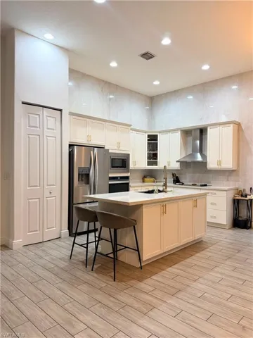 Spacious kitchen featuring an island with countertop seating, stainless steel appliances, recessed lighting, wood-look plank flooring, and a full-height tile backsplash