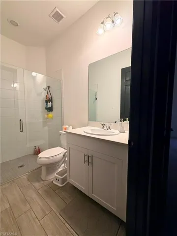Bathroom featuring a glass-enclosed shower with tile surround, white vanity with integrated sink, rectangular mirror, and wood-finish tile flooring