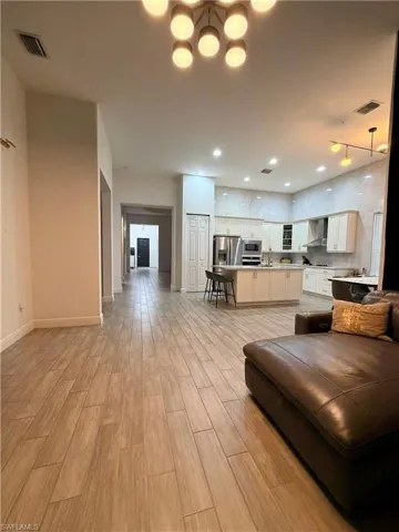 Open-concept interior featuring wood-finish flooring, a modern kitchen with a central island, stainless steel appliances, and sleek overhead lighting