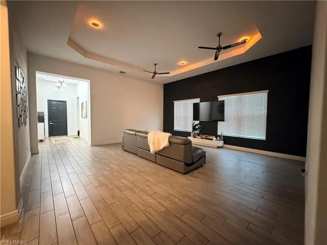 Spacious living area featuring wood-finish tile flooring, a tray ceiling with recessed lighting, and dual ceiling fans