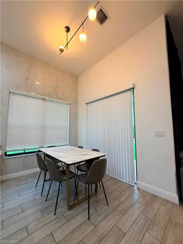 Dining area featuring a modern linear chandelier with globe lights, a large window with blinds, and a glass sliding door