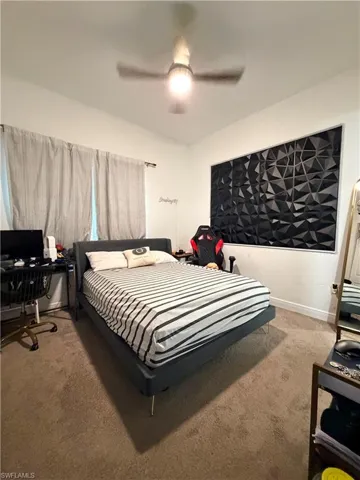 Carpeted room with a ceiling fan light fixture and a window featuring drapes