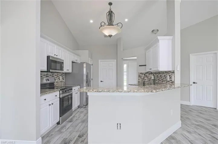Kitchen with decorative light fixtures, stainless steel appliances, kitchen peninsula, and light wood-type flooring