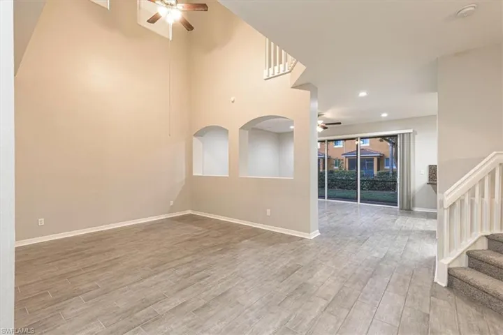 Unfurnished living room featuring ceiling fan, stairway, light wood finished floors, a high ceiling, and recessed lighting