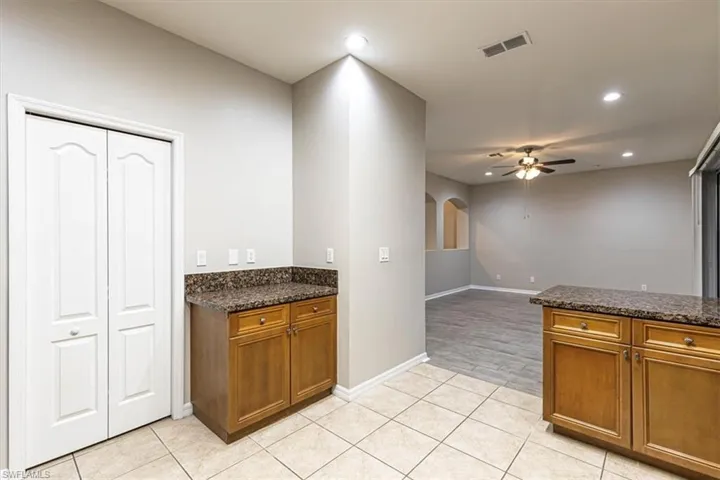 Kitchen featuring brown cabinetry, dark stone counters, recessed lighting, arched walkways, and ceiling fan