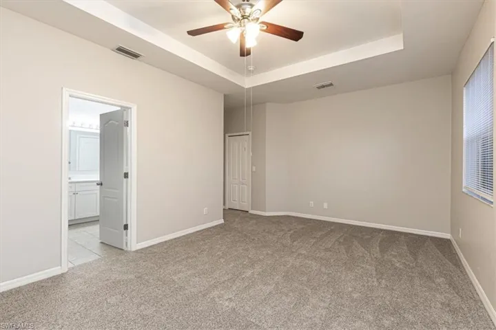 Unfurnished bedroom featuring a tray ceiling, light carpet, ceiling fan, and ensuite bath