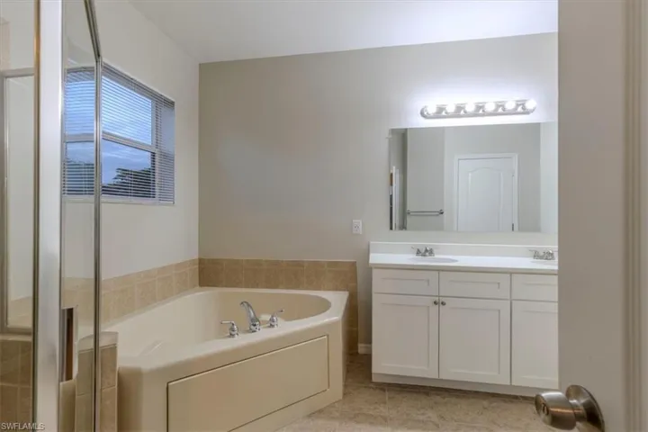 Bathroom featuring a bath, double vanity, light tile patterned flooring, and a shower with door