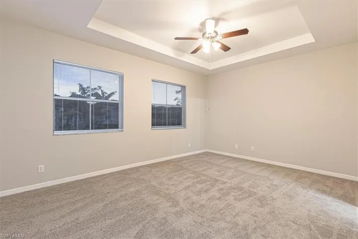 Spare room featuring a raised ceiling, light colored carpet, and a ceiling fan