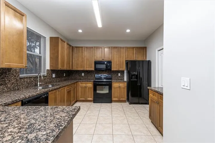 Kitchen with black appliances, dark stone counters, brown cabinets, light tile patterned flooring, and tasteful backsplash