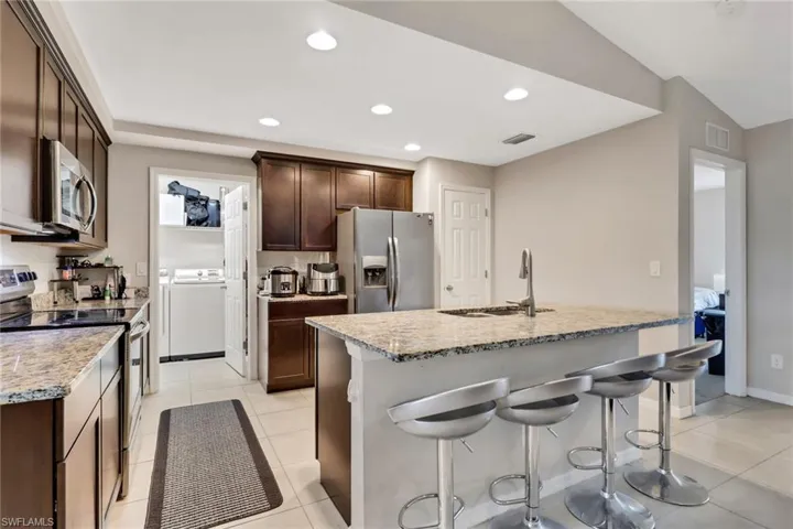 Kitchen with stainless steel appliances, dark brown cabinets, a kitchen breakfast bar, light stone counters, and recessed lighting
