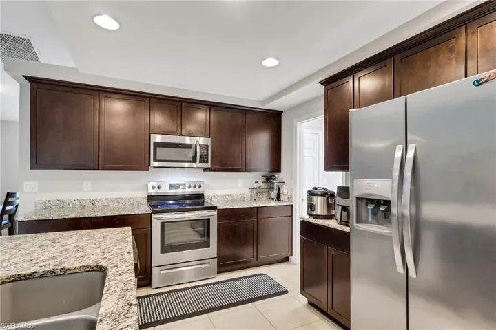 Kitchen with appliances with stainless steel finishes, light stone countertops, dark brown cabinetry, light tile patterned floors, and recessed lighting