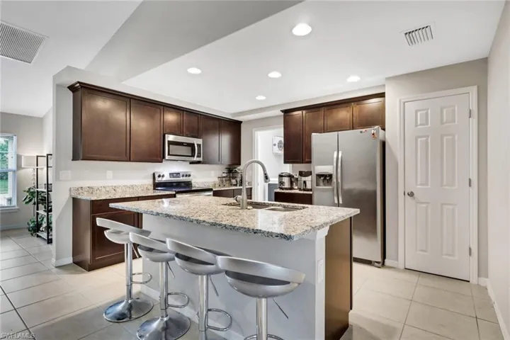 Kitchen with dark brown cabinetry, stainless steel appliances, a breakfast bar, light stone countertops, and recessed lighting