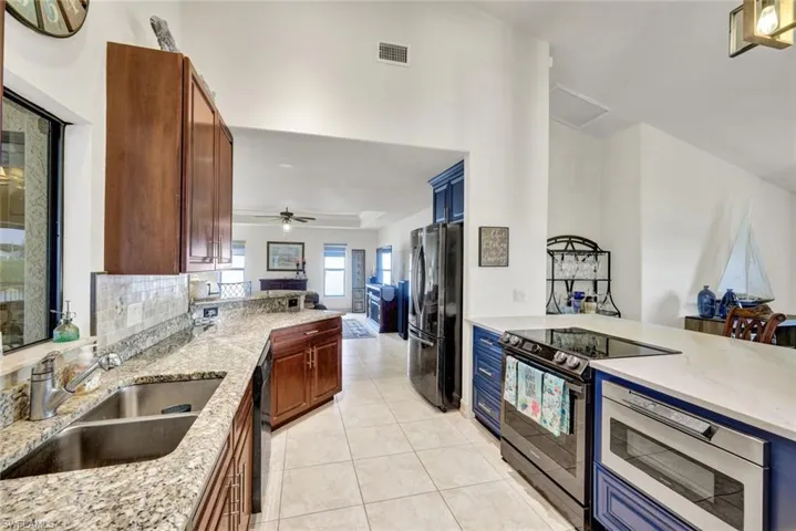 Kitchen with black appliances, light stone counters, a peninsula, open floor plan, and light tile patterned floors