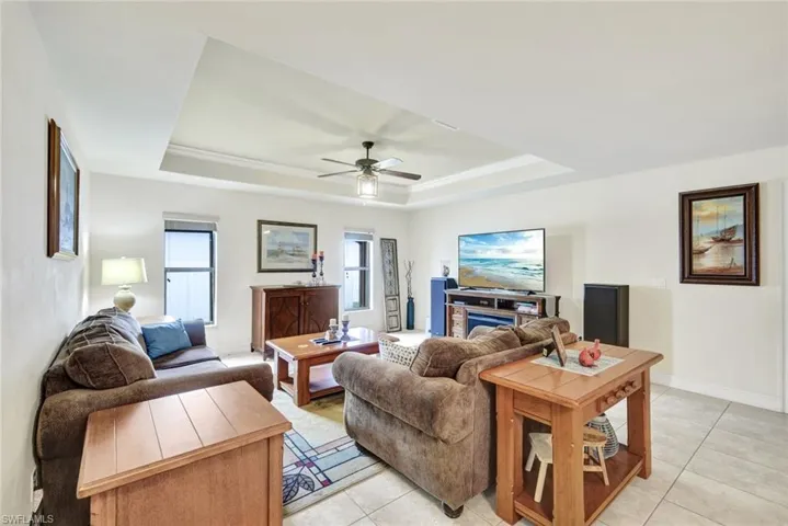 Living area featuring a raised ceiling, light tile patterned floors, and a ceiling fan