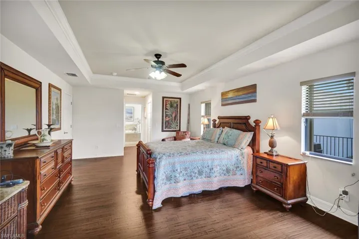 Bedroom with dark wood-style flooring, crown molding, a tray ceiling, ceiling fan, and connected bathroom