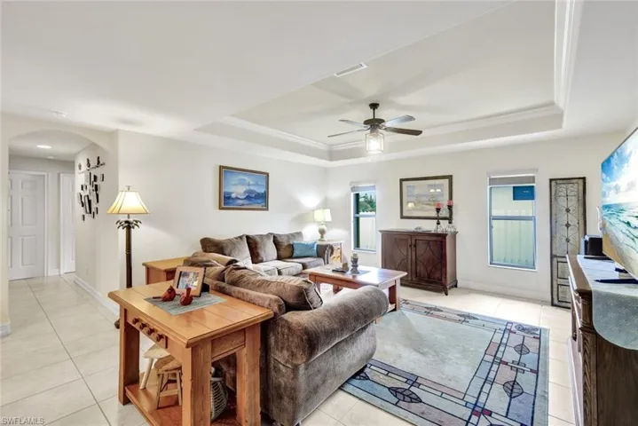 Living room with arched walkways, a raised ceiling, ceiling fan, and light tile patterned floors