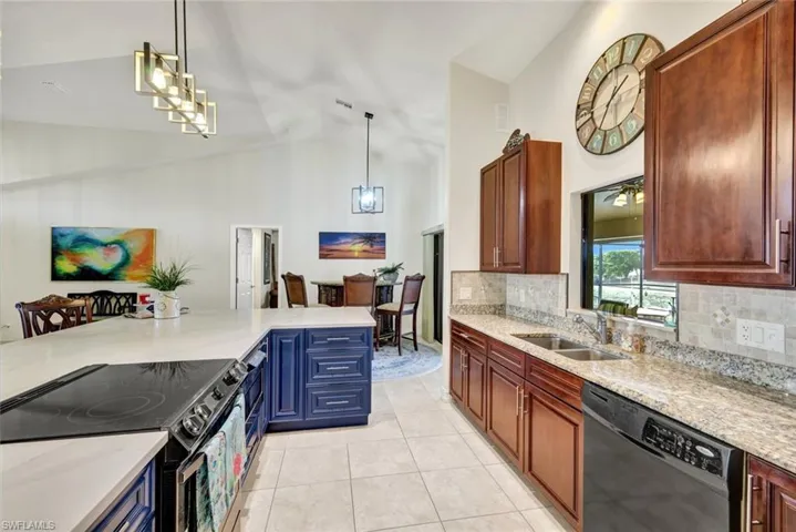 Kitchen featuring electric range, black dishwasher, pendant lighting, light stone countertops, and high vaulted ceiling