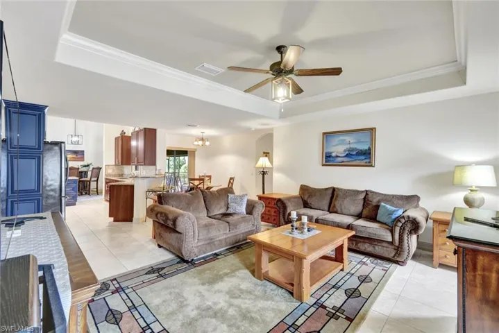 Living room featuring light tile patterned flooring, ornamental molding, a chandelier, a ceiling fan, and a raised ceiling