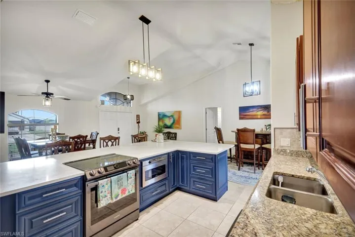 Kitchen featuring blue cabinetry, appliances with stainless steel finishes, pendant lighting, vaulted ceiling, and light stone counters