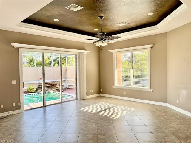 Tiled empty room featuring a textured ceiling, ceiling fan, a raised ceiling, and crown molding