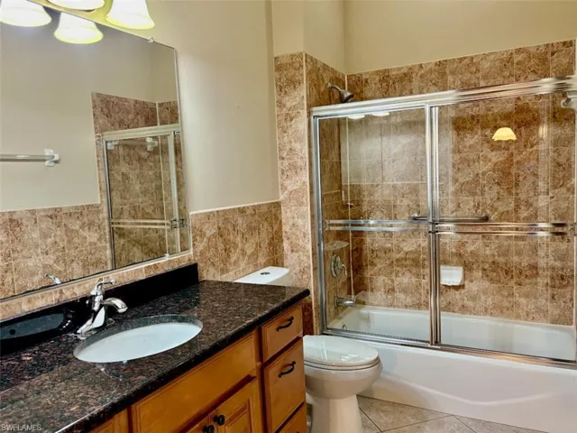 Full bathroom featuring vanity, tile patterned floors, toilet, enclosed tub / shower combo, and tile walls