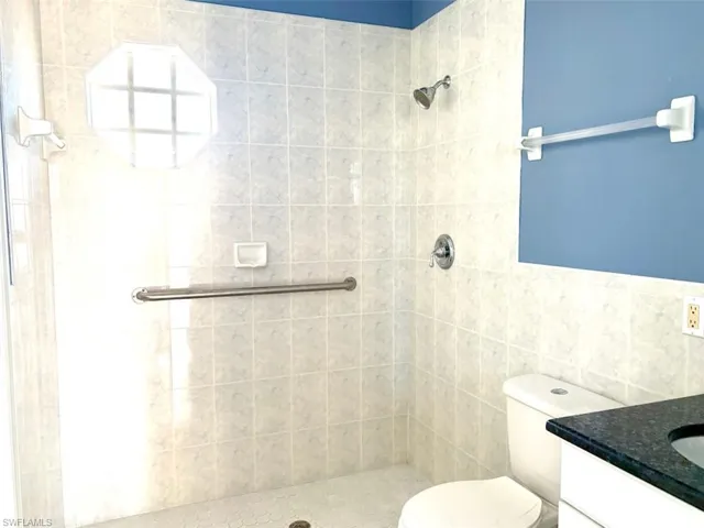 Bathroom featuring a tile shower, vanity, tile walls, and toilet