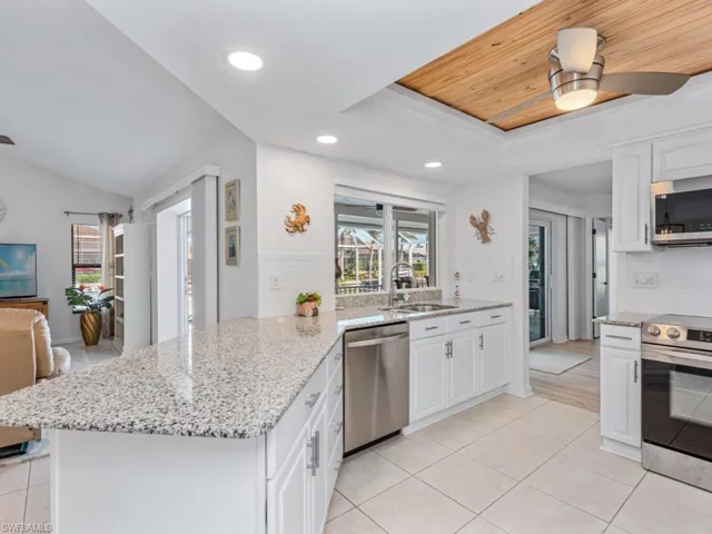 Kitchen with a peninsula, a sink, stainless steel appliances, white cabinets, and a raised ceiling