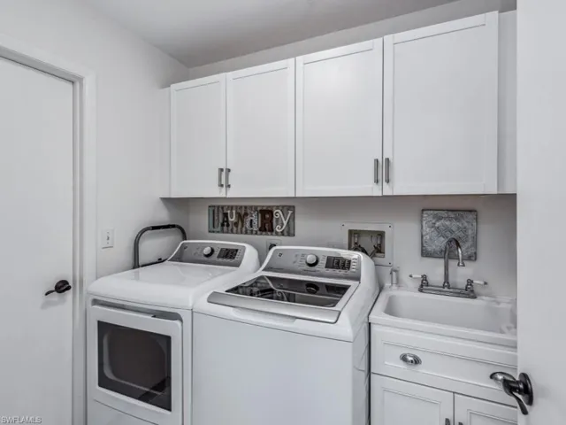 Clothes washing area featuring separate washer and dryer, sink, and cabinets