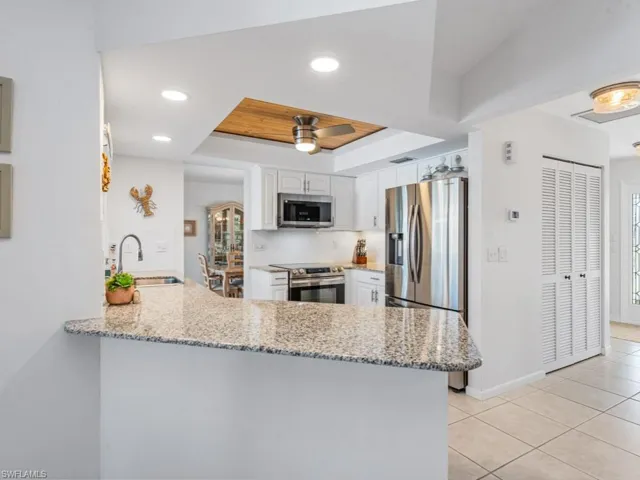 Kitchen featuring a peninsula, a sink, appliances with stainless steel finishes, white cabinetry, and a raised ceiling