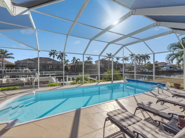 View of swimming pool featuring glass enclosure, a water view, and a patio