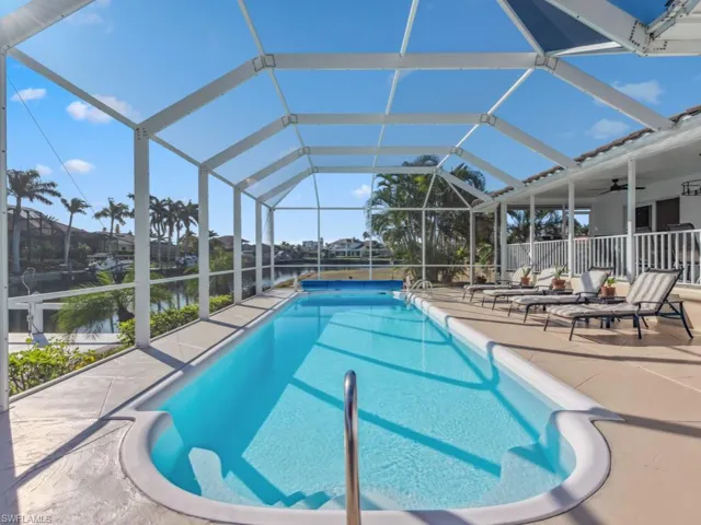 View of pool featuring glass enclosure, ceiling fan, a water view, and a patio
