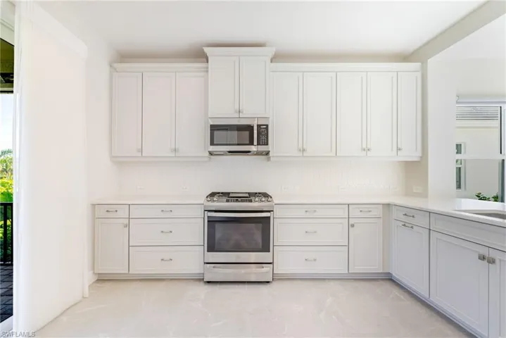 Kitchen with plenty of natural light, stainless steel appliances, white cabinets, and light stone countertops