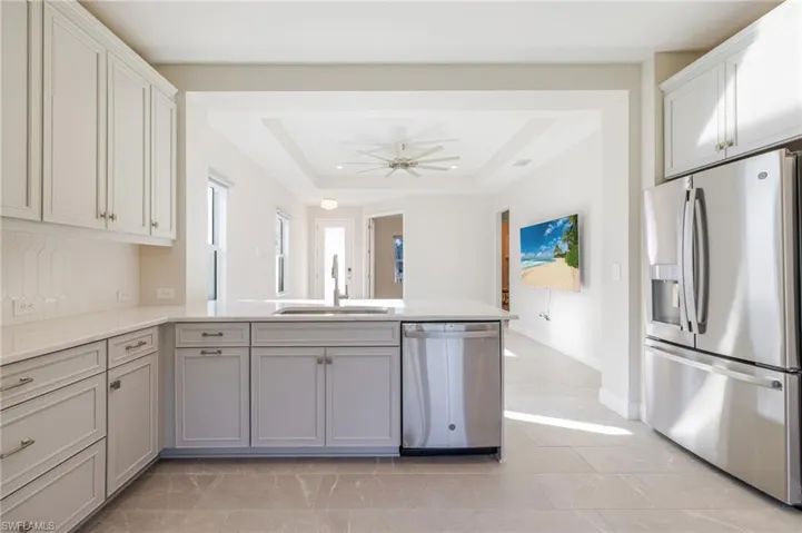 Kitchen featuring appliances with stainless steel finishes, a raised ceiling, light stone counters, a peninsula, and decorative backsplash