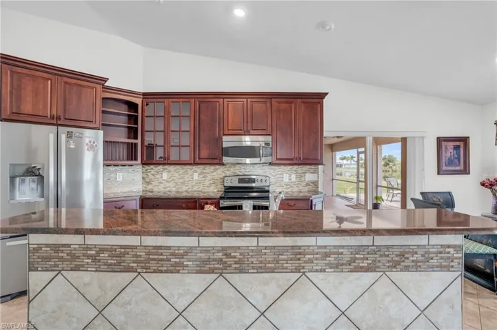 Kitchen featuring decorative backsplash, appliances with stainless steel finishes, vaulted ceiling, and light tile patterned floors